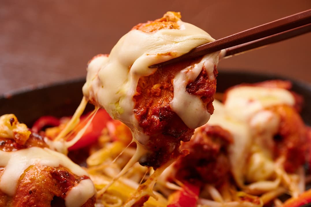 Cheese-topped grilled chicken and vegetables lifted with chopsticks at Sakura Asian Dining & Bar